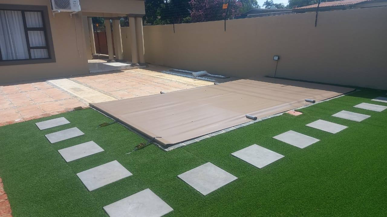 Beige PVC pool cover installation with landscaped garden and stepping stones